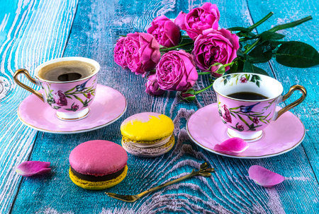 Two cups of coffee with pink roses and macaroons on blue wooden backgroundの写真素材