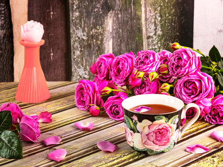 cup of tea with pink roses and petals on a wooden backgroundの写真素材