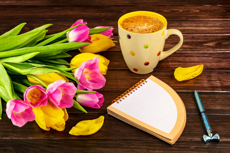 Cup of coffee with tulips and note book on wooden backgroundの写真素材
