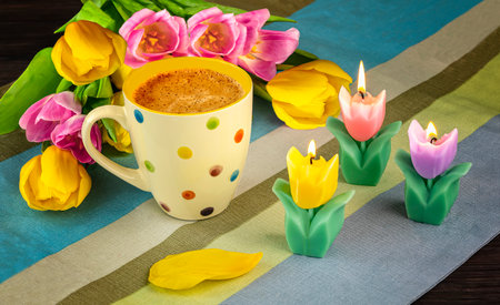 Cup of coffee with tulips and candles on a wooden backgroundの写真素材