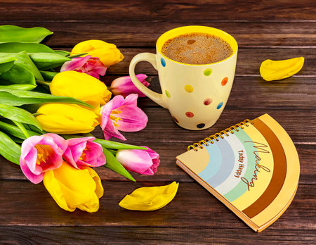 Cup of coffee with yellow tulips and notebook on wooden backgroundの写真素材