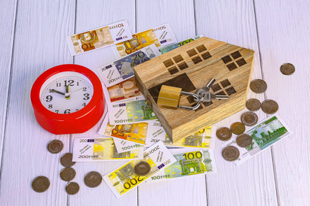 House model, alarm clock and euro banknotes on white wooden background. Home loan concept.の写真素材