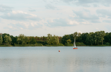 Sailboat or yacht on a lake in nice weather and blue sky. Sailing boat on a calm lake with reflection in the water.の写真素材