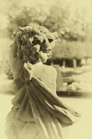Old statue of an infant angel or cupid in the garden. Guardian angel statue in sunlight as a symbol...