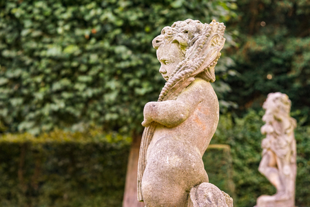 Old statue of an infant angel or cupid in the garden. Guardian angel statue in sunlight as a symbol of love in garden.の写真素材