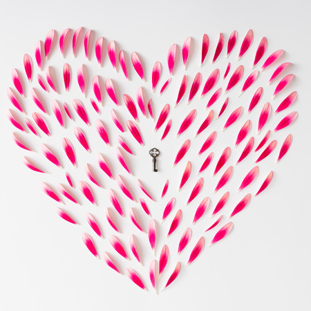 Heart symbol made of pink flower petals with old key. Flat lay.の写真素材