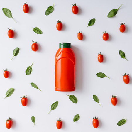 Ketchup bottle concept with cherry tomatoes and basil leaves pattern. Flat lay.の写真素材