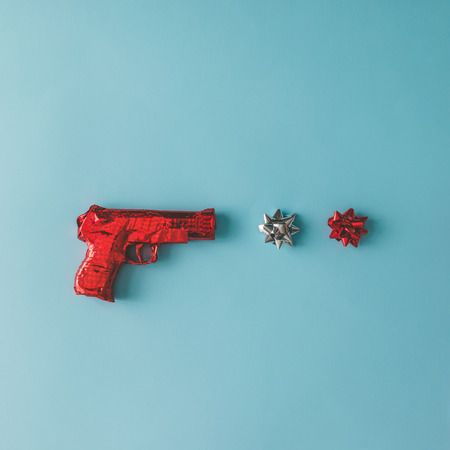 Gun wrapped in red paper with bows on blue background. Flat lay Christmas concept.の写真素材