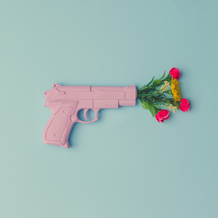 Pink hipster handgun on blue pastel background with flowers. Piece flat lay concept.の写真素材