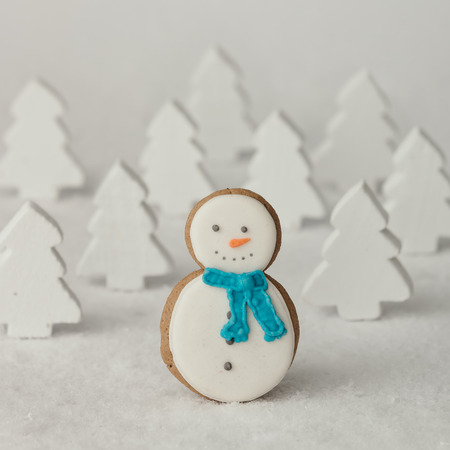 Gingerbread snowman Christmas cookie in front of snowy pine trees. Holiday concept.