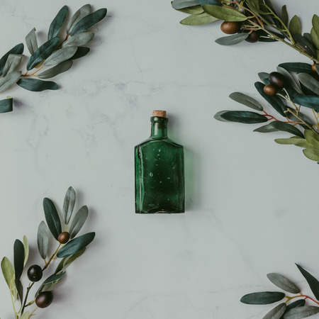 Creative mock up layout made of olive branches with green bottle on table. Homemade flat lay concept.の写真素材