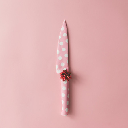 Knife wrapped in dotted paper with bow on pink background. Flat lay Christmas concept.