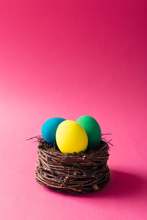 Colorful Easter eggs in bird nest on pink backgroundの写真素材