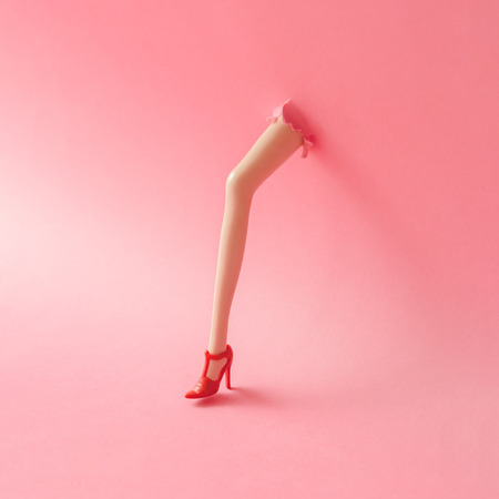 Doll leg on high heels breaking through pastel pink wall. Creative minimal concept.の写真素材