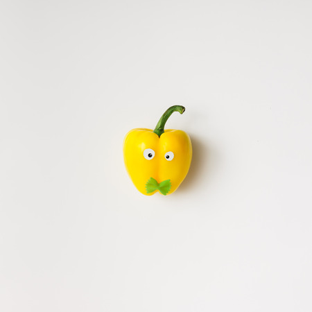 Yellow pepper with eyes and bowtie on white background. Minimal conceptの写真素材