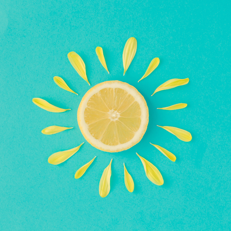 Sun made of lemon and yellow flower petals on bright blue background. Fruit summer minimal concept.の写真素材