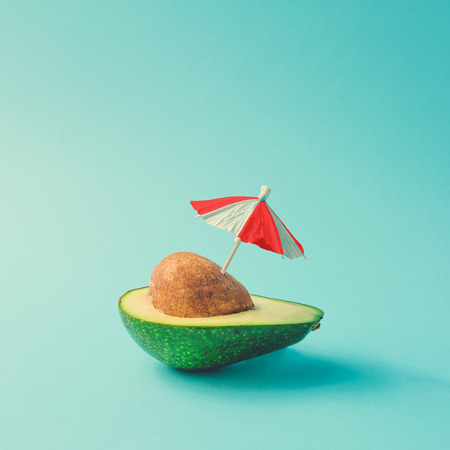 Tropical beach concept made of avocado fruit and sun umbrella. Creative minimal summer idea.