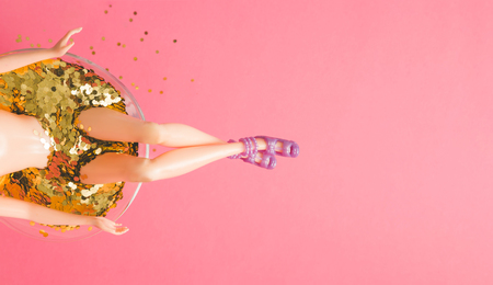 Doll bathing in martini glass full of gold glitter on pink background. Creative minimal beauty summer concept. Top view.の写真素材