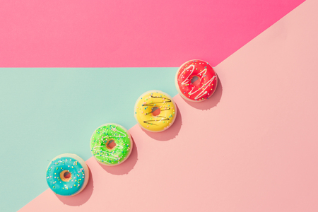 Creative arrangement of colorful donuts on pastel pink and blue background. Minimal food concept. Flat lay.の写真素材