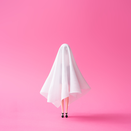 Girl in ghost costume against pastel pink background. Halloween party minimal concept.の写真素材