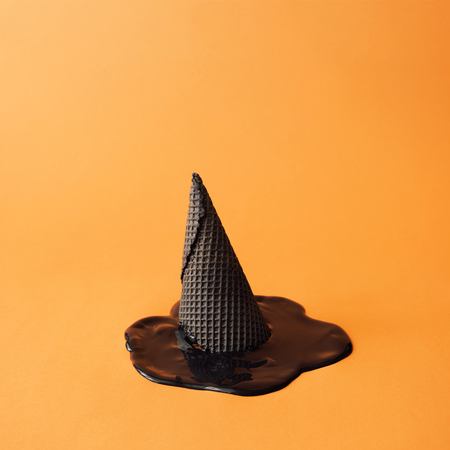 Witch hat made of black ice cream cone with melted black ice cream on orange background. Halloween minimal concept.の写真素材