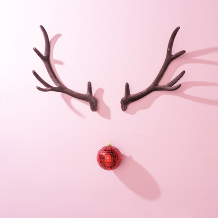 Red Christmas disco ball bauble with reindeer antlers on pink background. Minimal New year Santa concept. Flat lay.の写真素材