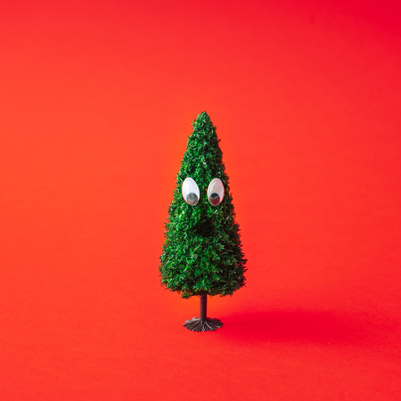 Christmas tree with googly eyes on red background. Minimal New Year fun concept.の写真素材