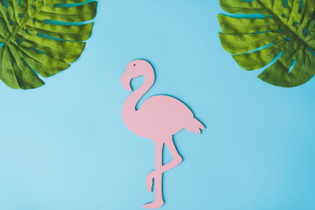 Pink flamingo shape with green tropical leaves on bright blue background. Summer tropical composition with copy space. Flat lay minimal. Summer Holiday layout.の写真素材