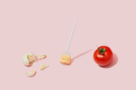 Minimal food concept with fork with spaghetti pasta, tomato and garlic against pastel pink...