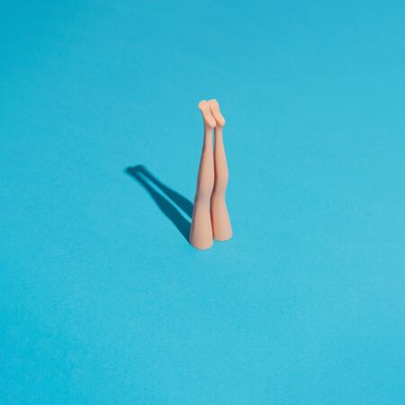 Minimal composition with doll legs and blue background. Sun and sharp shadows. Summer pool or sea diving concept. Vacation and relax inspiration.の写真素材