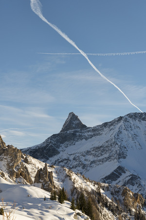 Rocky summit winter landscape with crossed contrails in the skyの写真素材