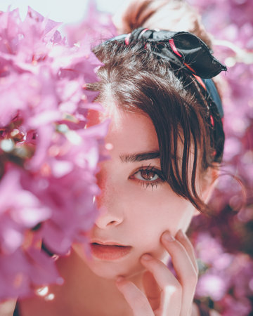 Portrait of a womanposing with her hand on her cheek among pink flowersの写真素材