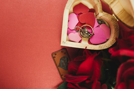 A heart-shaped box with hearts, a ring and red roses.