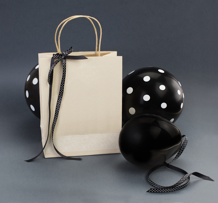 Recycled paper bag decorated with black satin ribbon. Black balloons, on grey background.の写真素材