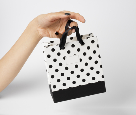 Female hand holding a white gift bag, with white polka dots on it. White background.の写真素材