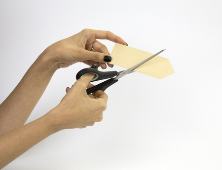 Female hand with black nails, holding scissors and cutting a price tag. Isolated on grey background.の写真素材
