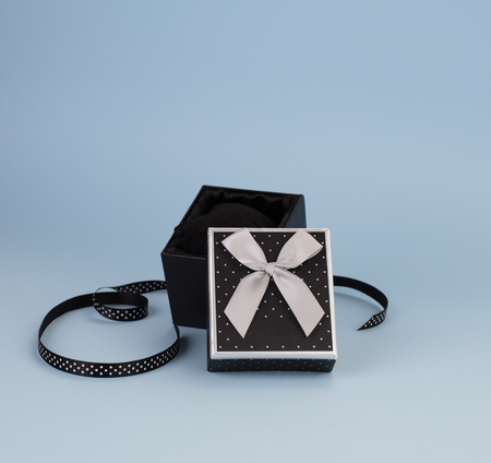 A black box, with an open lid; satin ribbon with polka dots next to it. Grey background.の写真素材