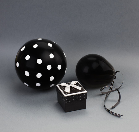 Two black balloons (one of them with white polka dots on it) and a black box with a grey satin bow on a lid. Grey background.の写真素材