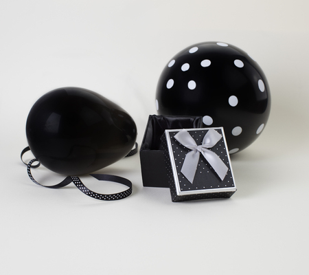 Two black balloons (one of them with white polka dots on it) and a black box with an open lid. White background.の写真素材
