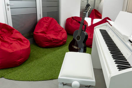 Modern music-room, with white piano and black guitar; red beanbags in the background.の写真素材