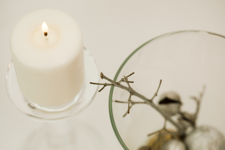 Winter composition â lit, white candle in glass candle-holder and silver decoration in glass vase. White background. Close-up.の写真素材