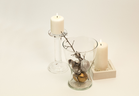 Winter composition â lit, white candle in glass candle-holder and silver decoration in glass vase. White background.の写真素材