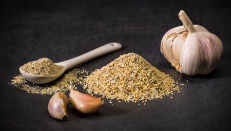 Garlic spice for recipes. Spoon and a pile of garlic powder. Garlic head and cloves on the table.の写真素材