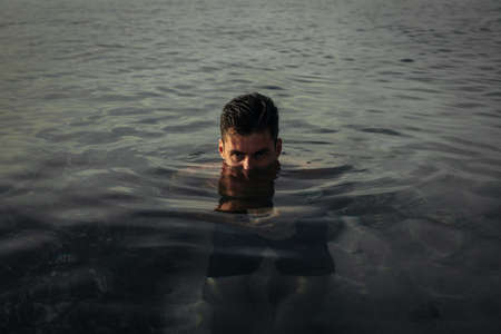 A handsome guy stands in the middle of the water on the beach