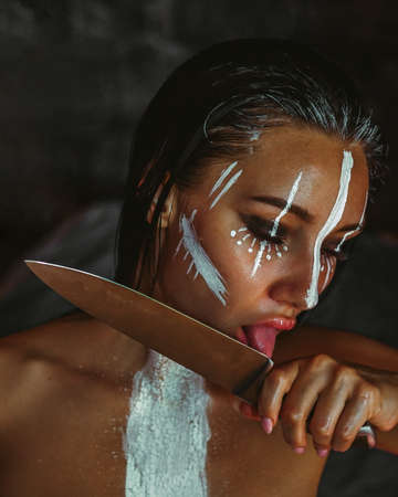 A brunette girl dangerously licks the blade of a knife