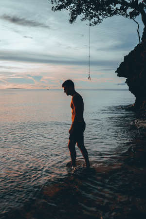 The guy enjoys the sunset riding on a swing on the ptropical beach. Silhouettes of a guy on a swing...