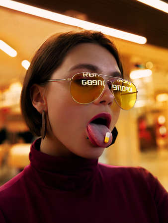 A girl with yellow glasses holding a pill on her tongue