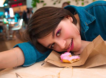 A girl eats a doughnut in a shopping center, leaning on a tableの写真素材