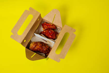 Chinese takeaway chicken with tomatoes, in a cardboard box photographed on a yellow backgroundの写真素材