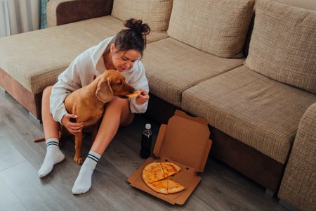 Girl sitting on the floor and feeding Cocker Spaniel pizza, leaning on the sofaの写真素材